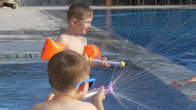 Father and two young brothers laugh while spraying water at each other with colorful water blasters in swimming pool. Family bonding, joyful childhood and unforgettable summer memories concept