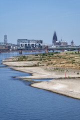 Naklejka premium Exposed gravel groynes and dried river bank of the Rhine in Germany due to a climate change drought. Cologne Cathedral and Kranhaeuser behind