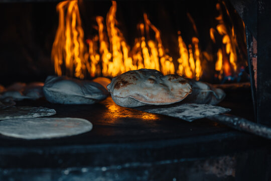 View of traditional local bread baking on a hot metal surface inside a wood-fired oven with visible flames in the background, Siwa, Marsa Matrouh Governo, Egypt.