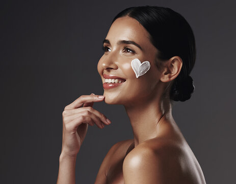 Radiant woman smiling with heart shaped moisturizing cream on her cheek.
