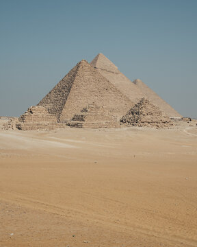 View of the ancient Giza Necropolis with the Great Pyramids rising above the desert sands under a clear blue sky in Al Haram, Giza Governorate, Egypt.
