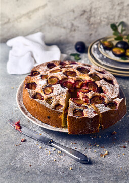 Sliced homemade plum cake on a ceramic plate with vintage knife and fresh fruits, rustic food photography