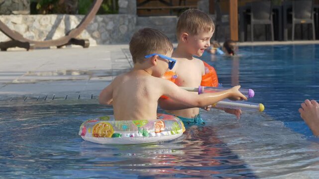 Father smiles while playing with two sons using water blasters in swimming pool. Warm family connection, shared happiness and quality time together concept. Positive parenting, joyful childhood