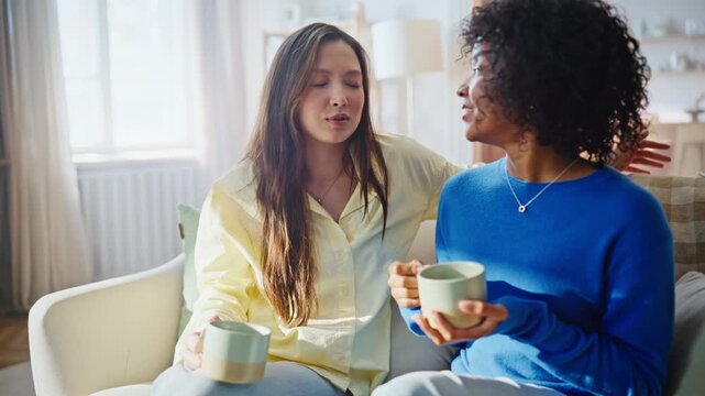 Woman comforting upset friend home sofa. Emotional support talk over coffee.