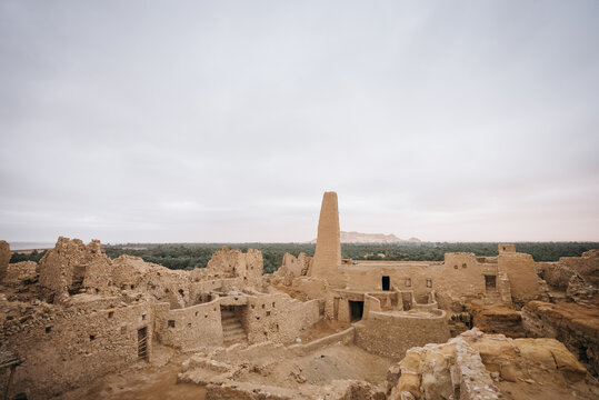 View of Amon Temple ruins with ancient mud-brick walls, stone structures, and palm groves in Siwa, Marsa Matrouh Governo, Egypt.