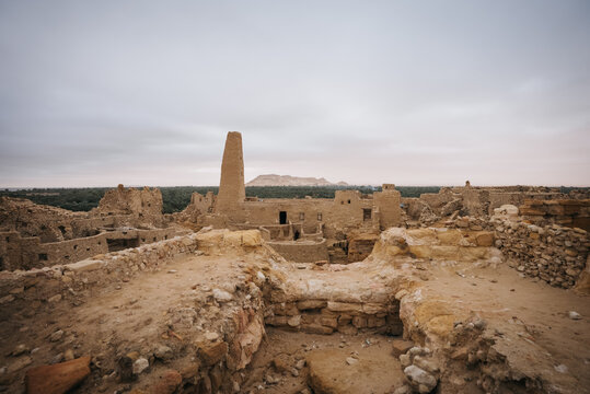 View of the ancient mud-brick ruins of the Amon Temple in the Siwa Oasis, with desert landscape and palm trees under an overcast sky in Siwa, Marsa Matrouh Governorate, Egypt.
