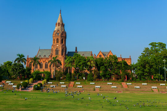 View of Government College University Lahore with its clock tower and red brick architecture, set against a clear blue sky with pigeons flying over the lawn, Lahore, Punjab, Pakistan.