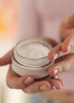 Woman applying face cream from cosmetic jar close up
