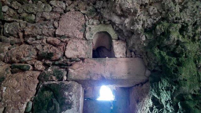 Xemxija, Malta 29.07.2026 - Heritage trail, Roman Baths, shelf like cut in the stone Dark cave walls show rough, textured surfaces. Greenish moss grows on damp, uneven stone. Light filters through nar