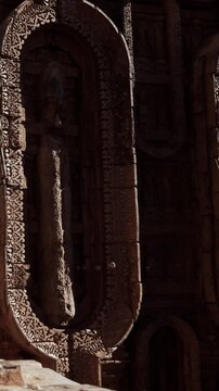 Stone structures are found in an ancient site with detailed carvings. Figures are visible on the stone walls. Shadows cast by the light add depth to the scene.