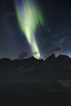 View of the aurora borealis illuminating the night sky above the rugged mountain peaks of Lofoten in Nordland, Norway.