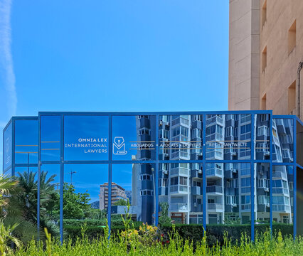Calpe, Spain - May 27, 2026.Modern office building OMNIALEX INTERNATIONAL LAWYERS reflecting high rise towers and greenery in Calpe, Spain on a sunny day
