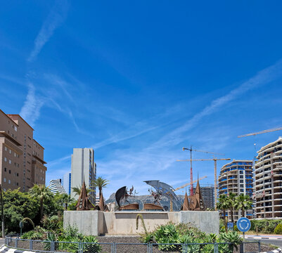 Urban roundabout view in Calpe, Spain featuring sculptures, palm trees, and modern buildings under a blue sky