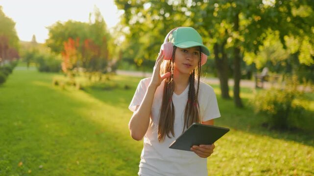 Relaxed Zoomer preteen listening to music holding tablet in the park.