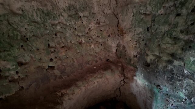 Ancient stone chamber, dimly lit, reveals worn, circular pit hole. Rough, mossy walls frame the dark, rocky opening, showing signs of age. No people or animals are visible, quiet