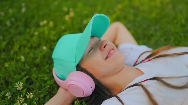 Smiling adolescent lying on green grass enjoying music outdoors.