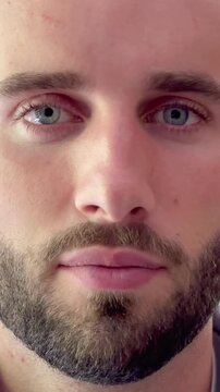 Extreme close-up of a handsome young bearded man's face opening his intense blue eyes and looking directly into the camera with a calm and focused expression, showcasing his features