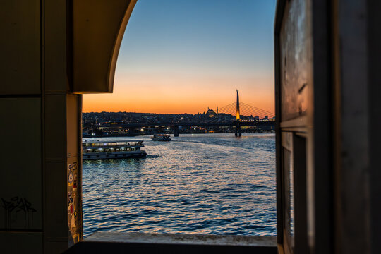 Golden Horn Metro Bridge and city skyline at sunset framed through a stone arch window at Istanbul, Turkey