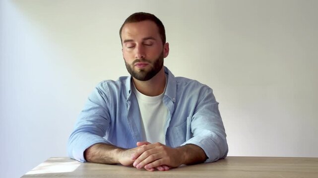 Bored and impatient young caucasian man with a beard waiting for someone while sitting at a wooden desk, isolated on a white background. His expression changes from bored to smiling at the end