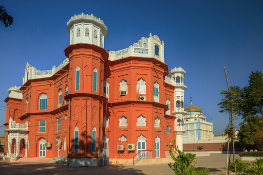 View of the vibrant orange palace with intricate white architectural details and arched windows under a clear blue sky in Pirjo Goth, Sindh, Pakistan.