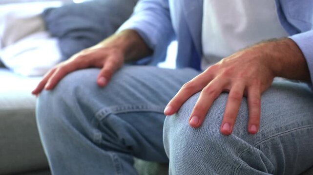 Close up view of a man's hands tapping his knees nervously while sitting on a couch, a subtle gesture of anxiety, impatience, stress, or anticipation showing his state of mind
