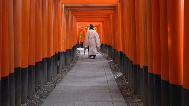 A Shinto priest walking through the iconic torii gates at Fushimi Inari Shrine in Kyoto, Japan, slow motion shot.