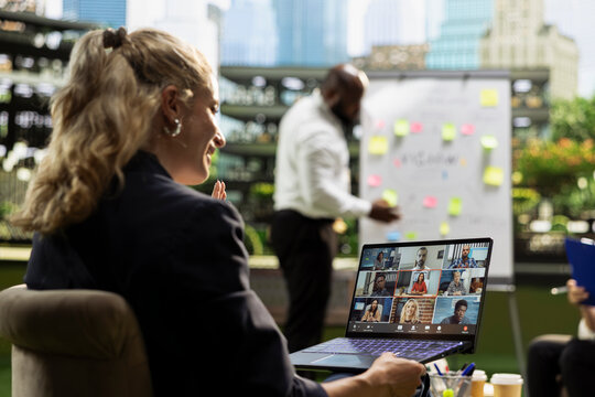 An employee joins a virtual meeting on a laptop for project planning and an online presentation during an outdoor work session in a business park.