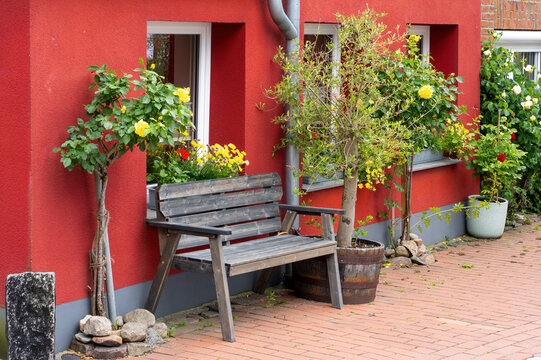 Wooden Bench in Front of Red House with Potted Plants and Flowers