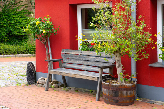 Wooden Bench in Front of Red House with Potted Plants and Flowers