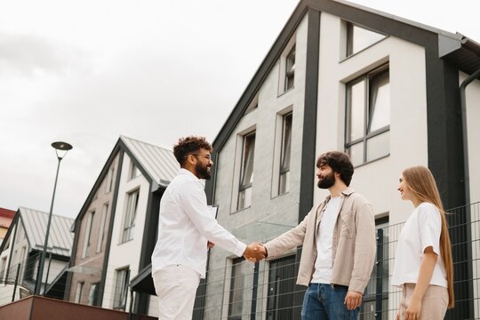 Realtor shaking hands with new homeowners outside house