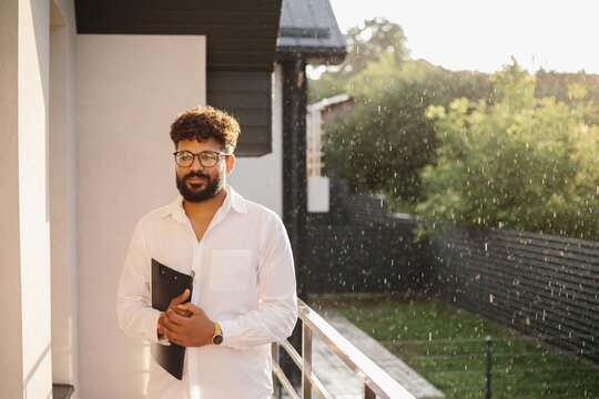 Male realtor holding clipboard on modern balcony