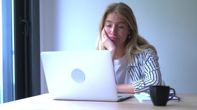 Overworked businesswoman feeling tired and bored while staring at her laptop screen in the office, struggling with a lack of motivation and showing signs of burnout at her workplace