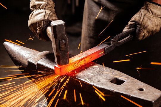 A close-up shot of a blacksmith striking glowing hot metal on an anvil, creating flying sparks.