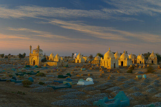 View of the historic Mian Nasir Kalhoro Graveyard with ancient domed tombs illuminated by the golden hour light in the desert landscape of Dadu, Sindh, Pakistan.