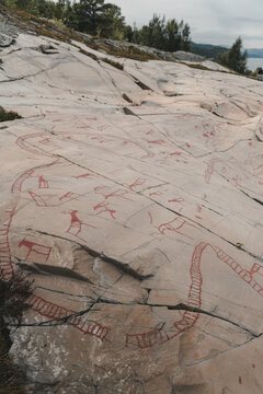 View of ancient red-painted rock carvings depicting animals and human figures on a smooth stone surface at the Alta Museum World Heritage Center for Rock Carvings in Alta, Finnmark, Norway.