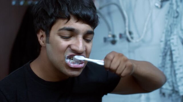 Young Indian man brushing his teeth early morning with a toothbrush  daily routine. Indian stock footage of a handsome man in brushing his teeth in the bathroom in front of the mirror