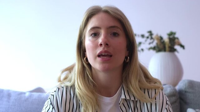 Confident young businesswoman speaking directly to the camera during an online conference call, actively gesturing while explaining her point of view from her modern living room