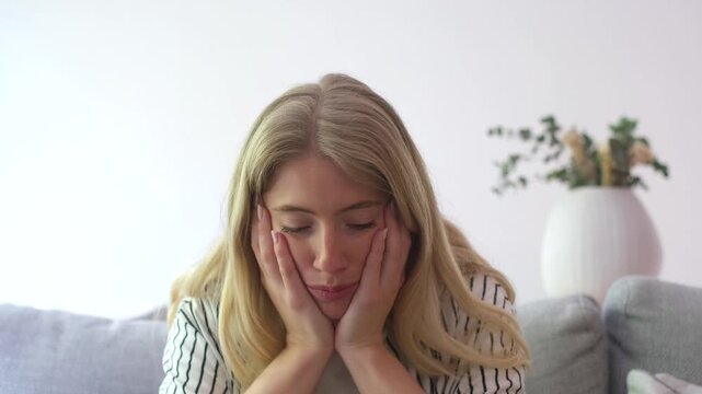 Young blonde woman showing a wide range of negative emotions, from disappointment and sadness to frustration and anger, while sitting on a couch in a living room, talking to someone off-camera