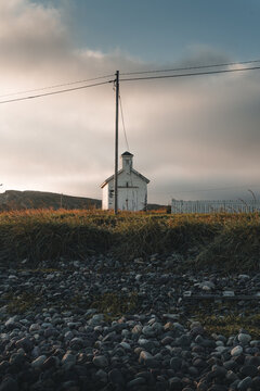 Kiberg, Finnmark, Norway - 25 August 2025: View of a small white building standing on a rocky beach under a soft sunset sky.
