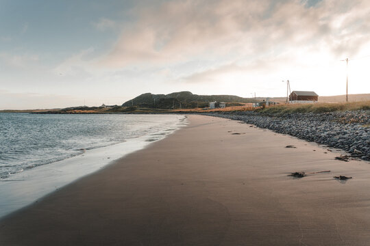 Kiberg, Finnmark, Norway - 25 August 2025: View of the sandy beach in Kiberg with a rocky shoreline, distant hills, and a small red building under a soft sky.