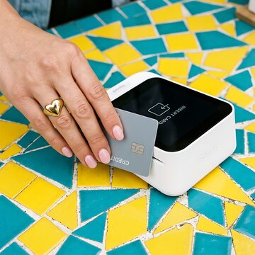 Woman using a credit card machine with a chip reader on a vibrant yellow and blue table.