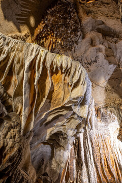 Low angle close up view of intricate stalactites and drapery speleothems inside an illuminated limestone cave