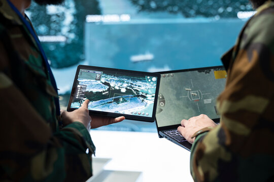 Army personnel compare target information on tablets in the command center; team members review tactical surveillance imagery across device screens during threat monitoring and defense planning.