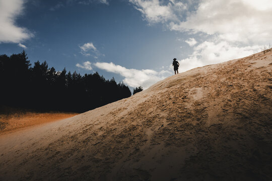 Piusa, Voru County, Estonia - 17 July 2024: View of a person standing on the sandy slopes of the Piusa sand dunes with a forest in the background under a blue sky.