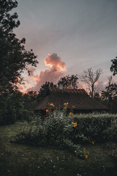 Laane County, Estonia - 13 September 2025: View of a traditional house with a thatched roof in Vormsi, surrounded by lush greenery and trees under a dramatic sunset sky.