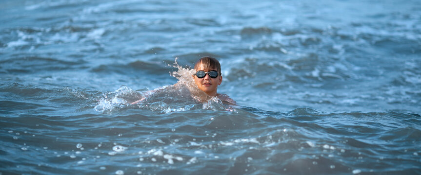 Boy swimming among sea waves in summer sunlight.