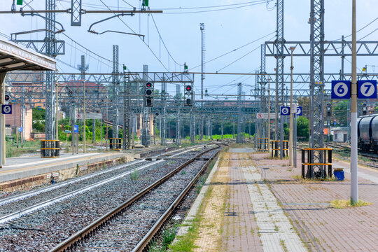 scenic view of an Italian train station featuring multiple empty railroad tracks, overhead electric power lines, and passenger platforms with track numbers six and seven under a clear sky.