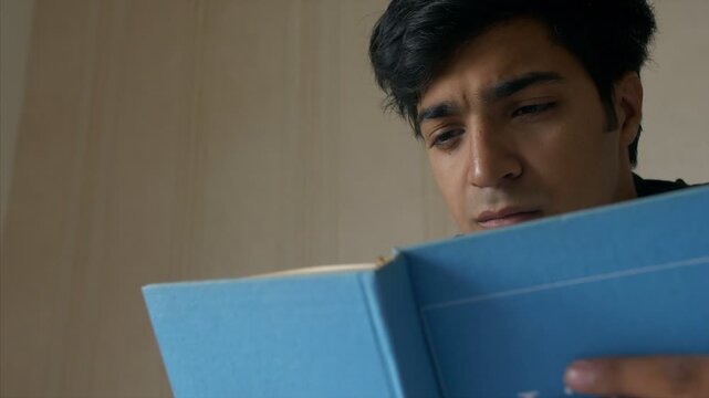 Smart teenager with weak eye-sight trying to read book with concentration . Indian stock footage of a charming boy in room holding a book trying to read without spectacles