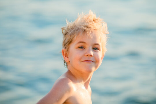 Portrait of a 5 to 6 year old blond boy by the sea in warm evening light.