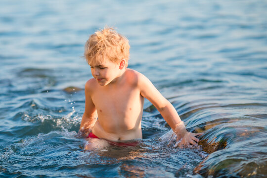 Young blond boy swimming in the sea with small waves around him.